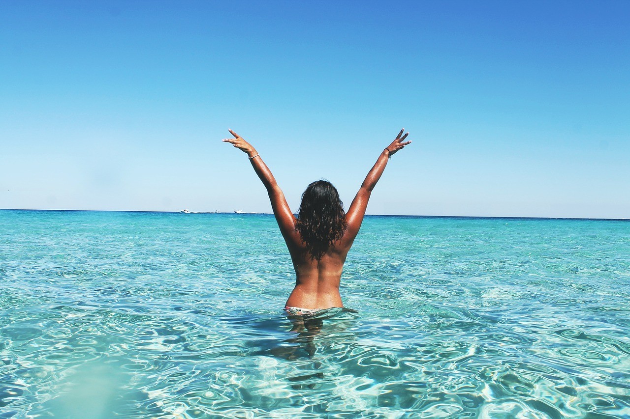 chica morena de espaldas con los brazos levantados en el mar